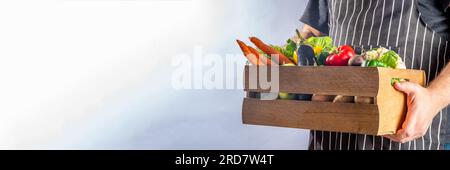 Concetto di shopping del mercato biologico agricolo, scatola di legno con estate, verdure crude e frutta autunnali, mani contadine su sfondo bianco Foto Stock