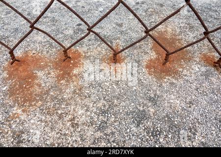 Dettaglio ravvicinato di una sezione una recinzione arrugginita delle maglie della catena e di come ruggine macchi la parete di cemento sottostante Foto Stock