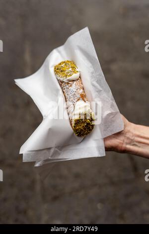 Cannoli siciliani freschi ripieni di ricotta e pistacchio tenuti da una donna Foto Stock