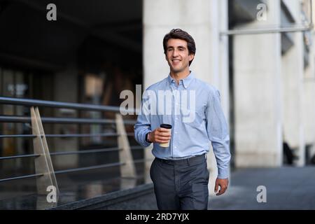 Felice giovane professionista che cammina con il caffè da asporto Foto Stock