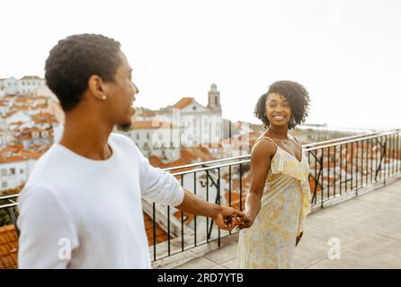 Allegro giovane ragazzo afro-americano che tiene la mano di una signora, una donna guida l'uomo in città, goditi un appuntamento e viaggia insieme Foto Stock