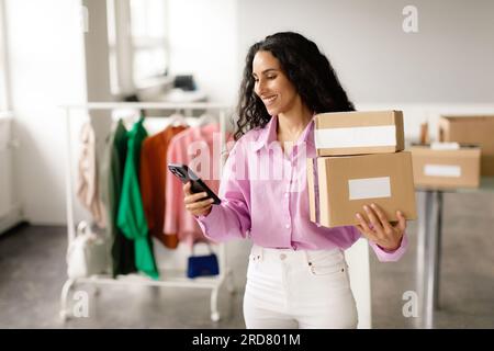 Messaggi da donna sullo smartphone con le scatole imballate al negozio di abbigliamento Foto Stock