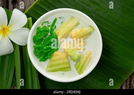 Vista dall'alto del dessert tailandese con foglie di panda seguite da foglie di banana verdi su fondo di legno. Foto Stock