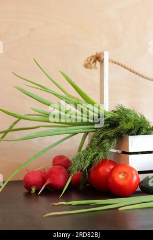 Cestino di legno con verdure fresche. Un mazzo di verdure in un cestino su un tavolo di legno. Cetrioli, pomodori, ravanelli, cipolle verdi e aneto Foto Stock