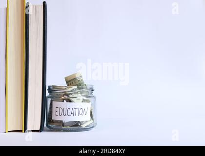 Vaso di vetro con denaro vicino a una pila di libri. Salvadanaio con dollari per l'istruzione. Risparmia denaro per i futuri studi universitari. Copia spazio Foto Stock