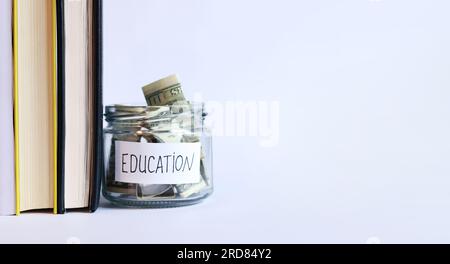 Vaso di vetro con denaro vicino a una pila di libri. Salvadanaio con dollari per l'istruzione. Risparmia denaro per i futuri studi universitari. Copia spazio Foto Stock