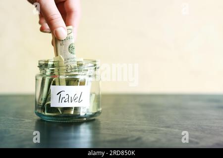 Salvadanaio con dollari per viaggiare. Vaso di vetro con soldi. La donna mette più soldi nel salvadanaio. Foto Stock