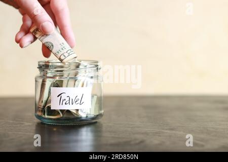 Salvadanaio con dollari per viaggiare. Vaso di vetro con soldi. La donna mette più soldi nel salvadanaio. Foto Stock