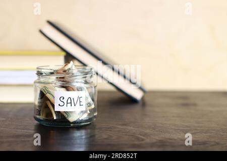 Risparmia denaro per il futuro. Vaso di vetro con dollari su un tavolo di legno sullo sfondo dei libri. Salvadanaio con banconote, spazio per le copie. Il concetto di Foto Stock