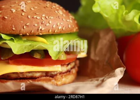 Succulento cheeseburger fatto in casa con polpettine, formaggio fuso, sottaceti, pomodoro e lattuga fresca. Primo piano sui fast food. Hamburger con panino di sesamo. Selettivo Foto Stock