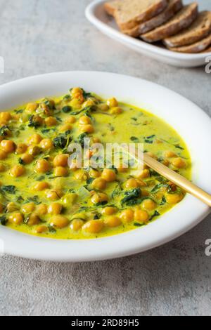 Pranzo sano e gustoso, zuppa con ceci e spinaci, spezie ed erbe fresche, con latte di cocco Foto Stock