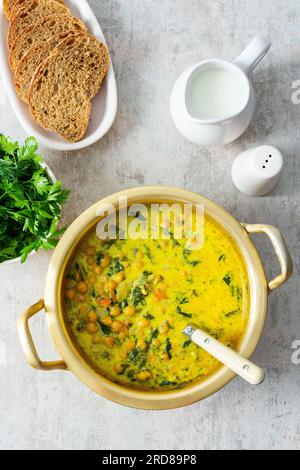 Pranzo sano e gustoso, zuppa con ceci e spinaci, spezie ed erbe fresche, con latte di cocco in padella Foto Stock