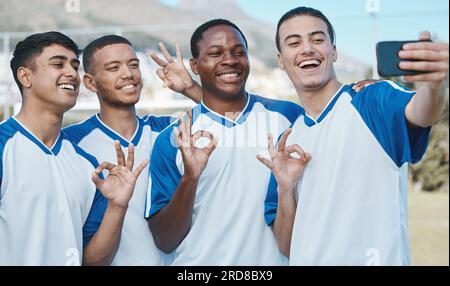 Uomini in selfie, OK mossa e competizione di calcio, sport e gruppo di atleti sul campo, diversità ed emoji. Felice, giovane giocatore di calcio maschile e squadra Foto Stock