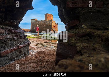 Vista da sotto di un uomo che si trova di fronte al castello di Torre Astura visto attraverso un buco nelle mura, provincia di Roma Foto Stock