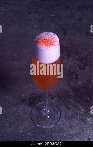 cocktail rinfrescante rosso con schiuma in un bicchiere su sfondo grigio. Foto Stock