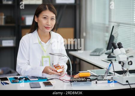 Ritratto di una giovane operaia che si occupa della riparazione e che smonta il telefono alla sua scrivania Foto Stock