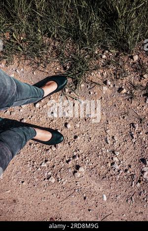 Foto verticale dall'alto verso il basso Vista delle gambe della donna in Black Ballet Flats su Country Road. Concetto di scarpe scomode per lunghe passeggiate. Foto Stock