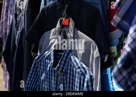 Le camicie multicolore sono appese agli appendiabiti del mercato. Primo piano. Foto Stock