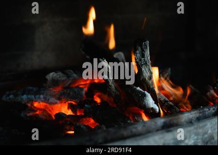 I tronchi di legno stanno bruciando nel caminetto. primo piano. Lingue di fiamma su sfondo scuro. Foto Stock