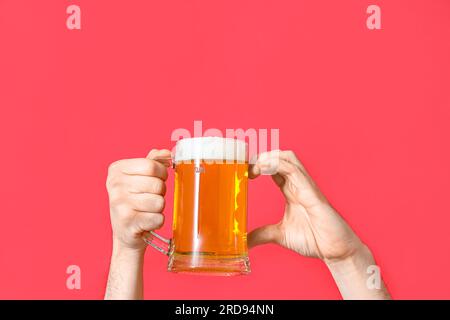 Mani maschili con tazza di birra fredda che mostrano gesti cardiaci su sfondo rosso Foto Stock