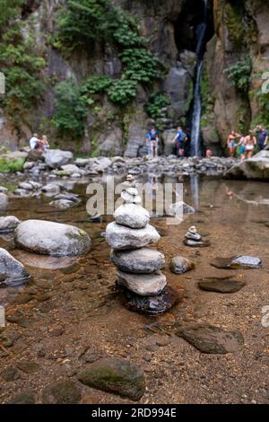 Un gruppo di zen pietre in un torrente circondato da turisti. Con la cascata del salto do Cabrito sullo sfondo. Isola di São Miguel nelle Azzorre Foto Stock