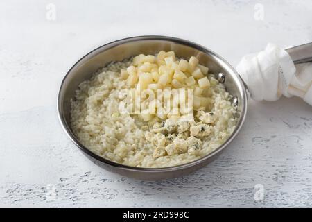 Friggere il risotto in padella, cucinare passo dopo passo, passaggio 6, aggiungere la pera e il formaggio blu su sfondo azzurro. Foto Stock