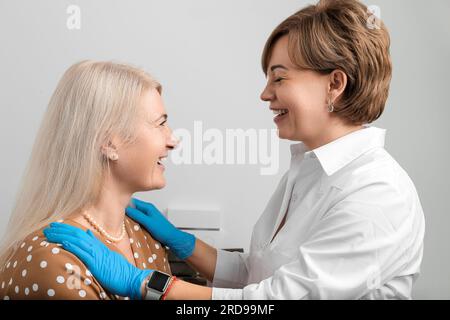 Consultazione in una clinica di cosmetologia. Il medico cosmetologo professionale e la donna adulta stanno sorridendo e discutendo le procedure per ringiovanimento Foto Stock