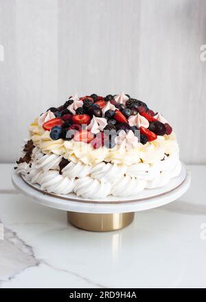 Torta Pavlova con formaggio panna montata, salsa al cioccolato e frutti di bosco freschi su sfondo grigio Foto Stock