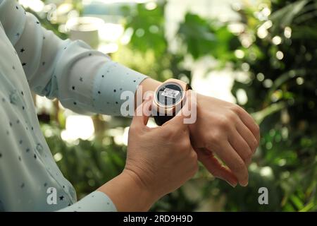 Donna che controlla il sistema di sicurezza domestica all'aperto tramite l'app smartwatch, primo piano. Immagine della stanza attraverso la telecamera CCTV sul display Foto Stock