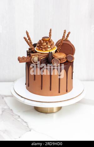 Torta al cioccolato riccamente decorata con dolci assortiti, cupcake, biscotti, barrette di cioccolato e macaron Foto Stock