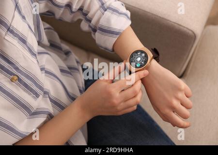 Donna che imposta il sistema di controllo della casa intelligente tramite smartwatch al chiuso, primo piano. Interfaccia app con icone sul display Foto Stock