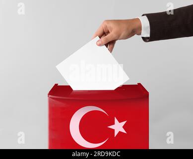 Uomo che mette il suo voto nelle urne decorate con la bandiera della Turchia sullo sfondo chiaro, primo piano Foto Stock