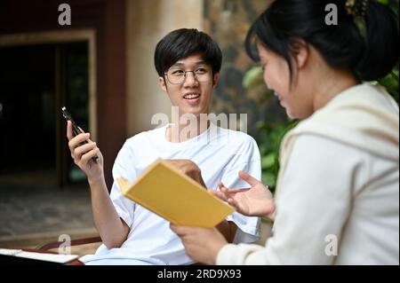 Un giovane asiatico felice ama parlare e rilassarsi a un tavolo in giardino con il suo amico nel fine settimana. Foto Stock