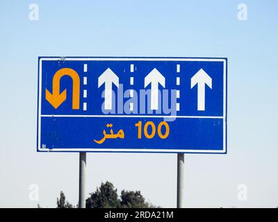 Traduzione del testo arabo (100 M cento metri) a lato di un cartello segnaletico informativo che mostra 4 corsie e indirizza i conducenti verso un u t Foto Stock