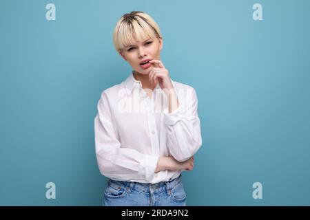 giovane donna bionda alla moda con taglio corto vestita con una camicia bianca su sfondo blu Foto Stock