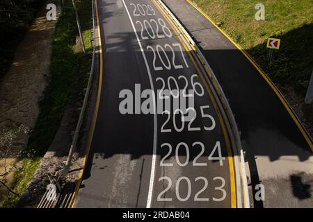 Gli anni dal 2023 al 2029 sono scritti sulla strada con una svolta a sinistra, la strada va in montagna nei Carpazi e lungo la strada che segue Foto Stock