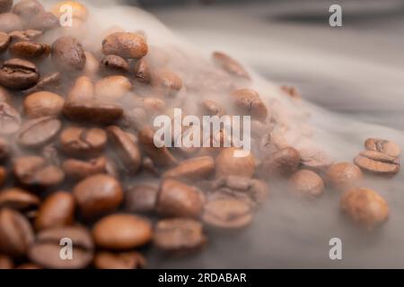 Tostatura di chicchi di caffè scuri, fumo e ombre, messa a fuoco morbida sullo sfondo Foto Stock