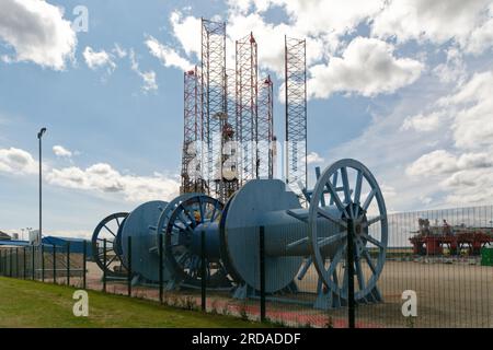 Grandi bobine di cavi blu in primo piano di un'area di costruzione di una piattaforma petrolifera a Invergordon, Scozia. Jack Up Rig Legs sullo sfondo. Foto Stock