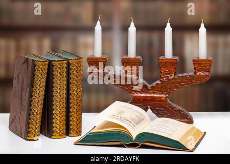 Libri antichi con un libro aperto davanti ad un antico candelabro di legno su un luminoso tavolo sopra la biblioteca astratta sfocata. Università, storia, memoria Foto Stock