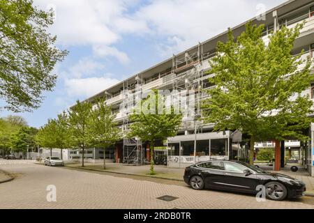 un condominio con auto parcheggiate sulla strada e alberi che fiancheggiano i marciapiedi davanti all'edificio c'è un cielo blu Foto Stock