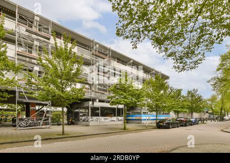 un edificio di appartamenti in città con molte auto parcheggiate sulla strada e alberi che fiancheggiano il lato della strada Foto Stock