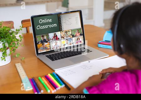 Ragazza birazziale che indossa le cuffie e partecipa a un corso online durante una videochiamata sul laptop a casa Foto Stock