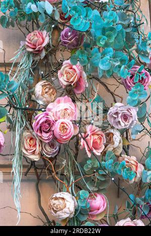 Fiori diversi e colorati artificiali e sfondo di foglie. Motivo di rose con rivestimento decorativo di foglie verdi sulla parete. Splendido fiore multicolore Foto Stock