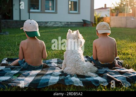 Ragazzi con un cane del West Highland White Terrier che mangiano cocomero sul prato del cortile. Foto Stock