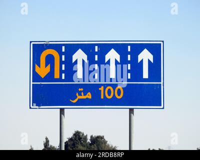 Traduzione del testo arabo (100 M cento metri) a lato di un cartello segnaletico informativo che mostra 4 corsie e indirizza i conducenti verso un u t Foto Stock