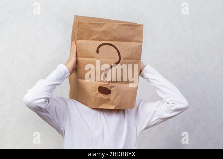 Uomo anonimo su sfondo grigio con una scatola di cartone sulla testa con un punto interrogativo disegnato. Problemi e soluzioni. Ottenere risposte. Foto Stock