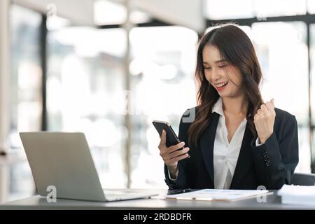 Donna d'affari di successo ed eccitante giovane donna entusiasta di vincere sul suo smartphone al lavoro Foto Stock