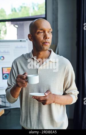 malattia cronica, inclusione, uomo afro-americano con malattia miastenia gravis tenendo tazza di caffè, audace e scura pelle ufficio lavoratore con ptosi Foto Stock