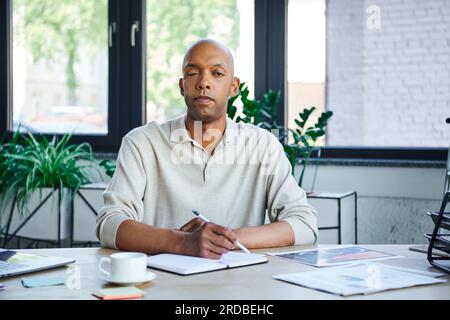 uomo con ptosi che prende appunti, coraggioso uomo d'affari afroamericano che guarda la fotocamera e tiene la matita, impiegato dalla pelle scura con miastenia grave Foto Stock