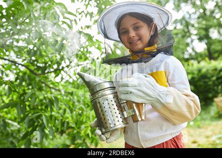 Ritratto di una ragazza sorridente che tiene un fumatore in piedi nel giardino dell'apiario Foto Stock